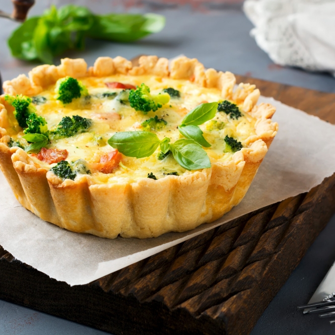 Homemade quiche tart with red fish salmon, broccoli, basil, seasonings and cheese on a gray stone background. Selective focus.